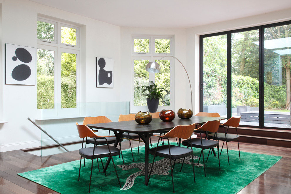 This is an example of a midcentury open plan dining room in London with white walls, dark hardwood flooring, no fireplace and feature lighting.