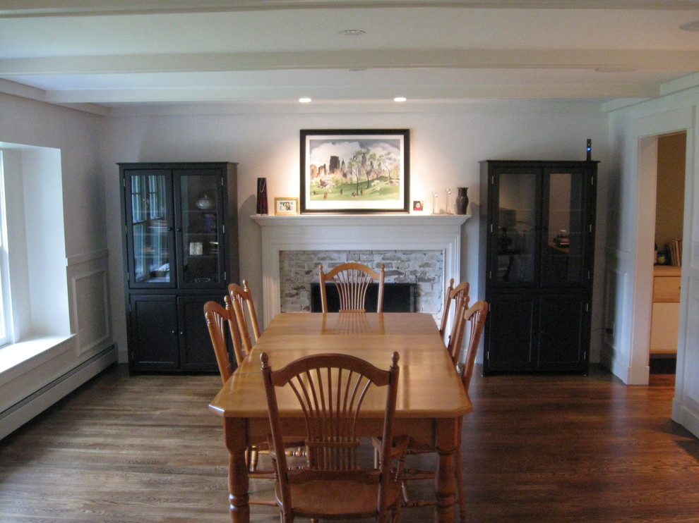 Cette photo montre une salle à manger chic fermée et de taille moyenne avec un mur gris, un sol en bois brun, une cheminée standard, un manteau de cheminée en brique et un sol marron.