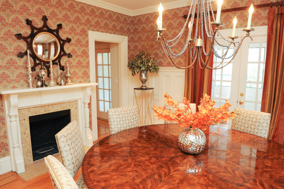 Immagine di una sala da pranzo chic chiusa e di medie dimensioni con pareti rosse, parquet chiaro, camino classico, cornice del camino in legno e pavimento arancione