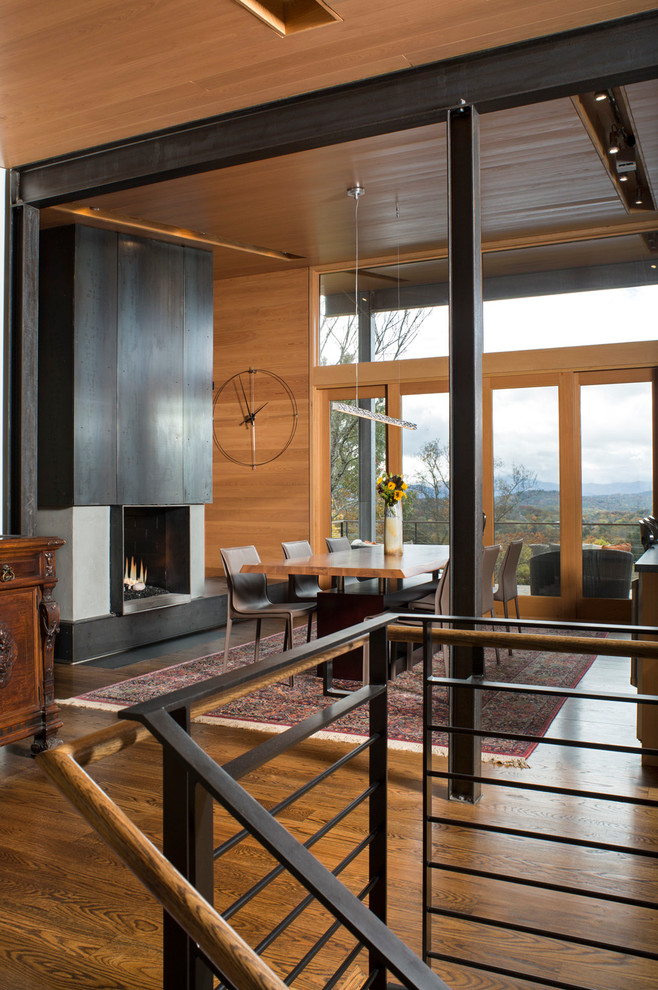 This is an example of a large contemporary kitchen/dining room in Charlotte with a two-sided fireplace, a metal fireplace surround, beige walls, dark hardwood flooring and brown floors.