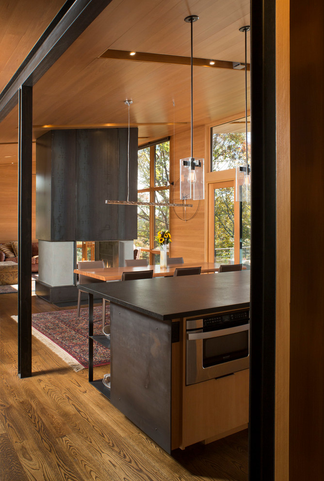 Aménagement d'une grande salle à manger ouverte sur la cuisine contemporaine avec une cheminée double-face, un manteau de cheminée en métal, un mur beige, parquet foncé et un sol marron.