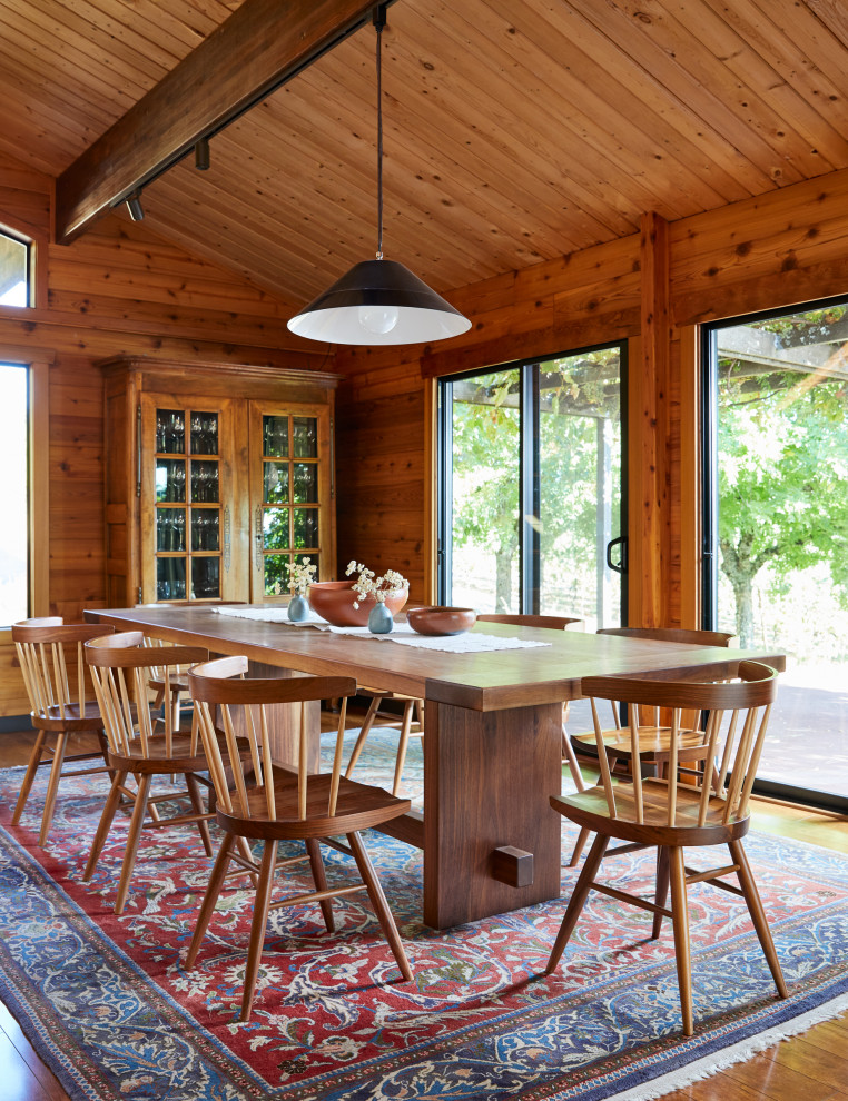 Cette image montre une grande salle à manger chalet en bois avec une cheminée standard, un mur marron, un sol en bois brun, un sol marron, un plafond voûté et un plafond en bois.