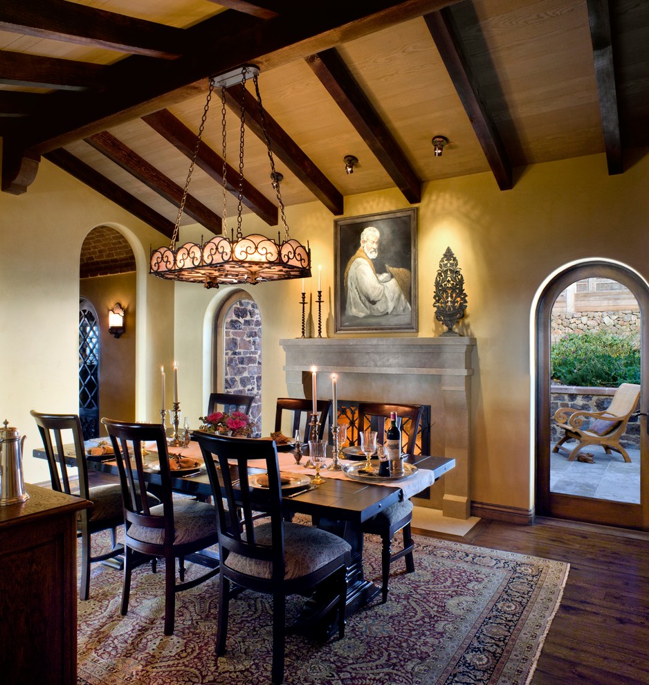 Photo of a rustic dining room in San Francisco with yellow walls, dark hardwood flooring and a standard fireplace.