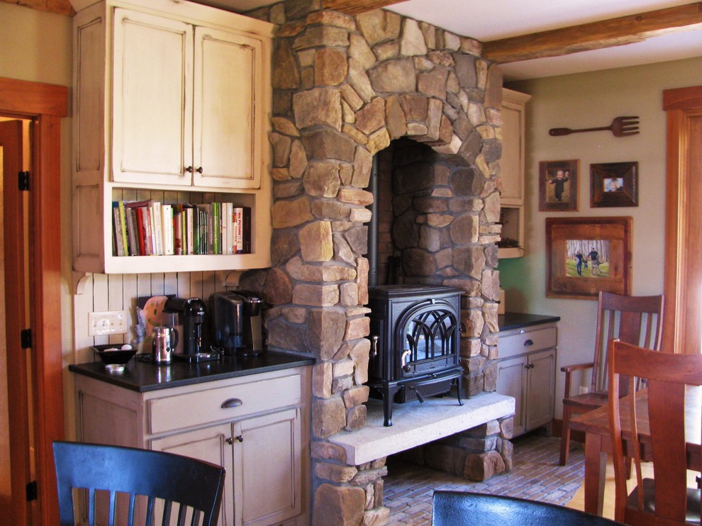 Пример оригинального дизайна: гостиная-столовая в стиле рустика с бежевыми стенами, кирпичным полом, печью-буржуйкой и фасадом камина из камня