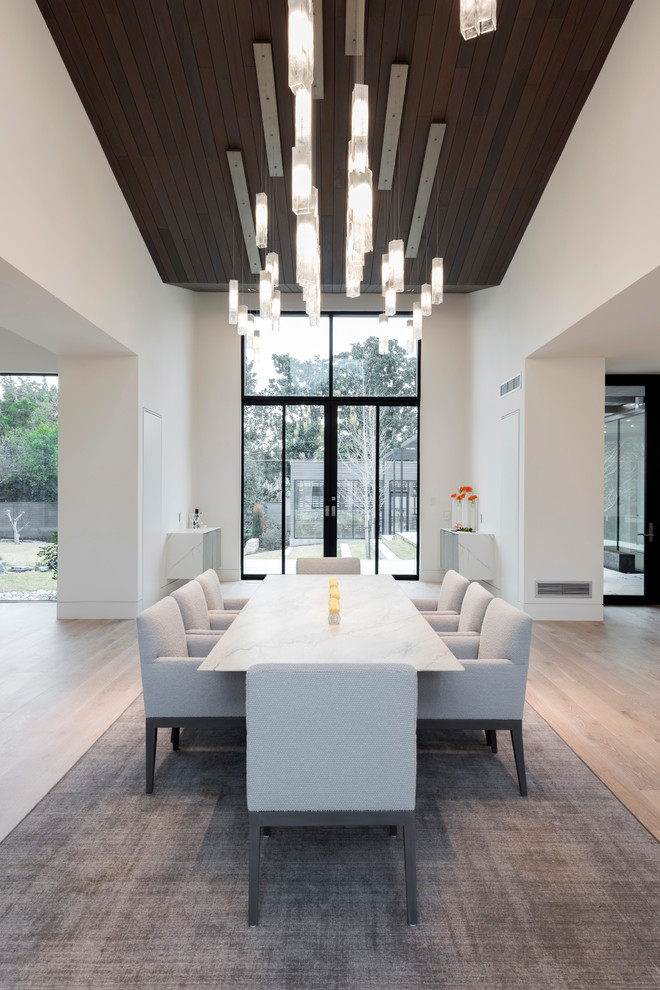 Cette image montre une très grande salle à manger ouverte sur la cuisine design avec un mur blanc, parquet clair, une cheminée standard et un manteau de cheminée en pierre.