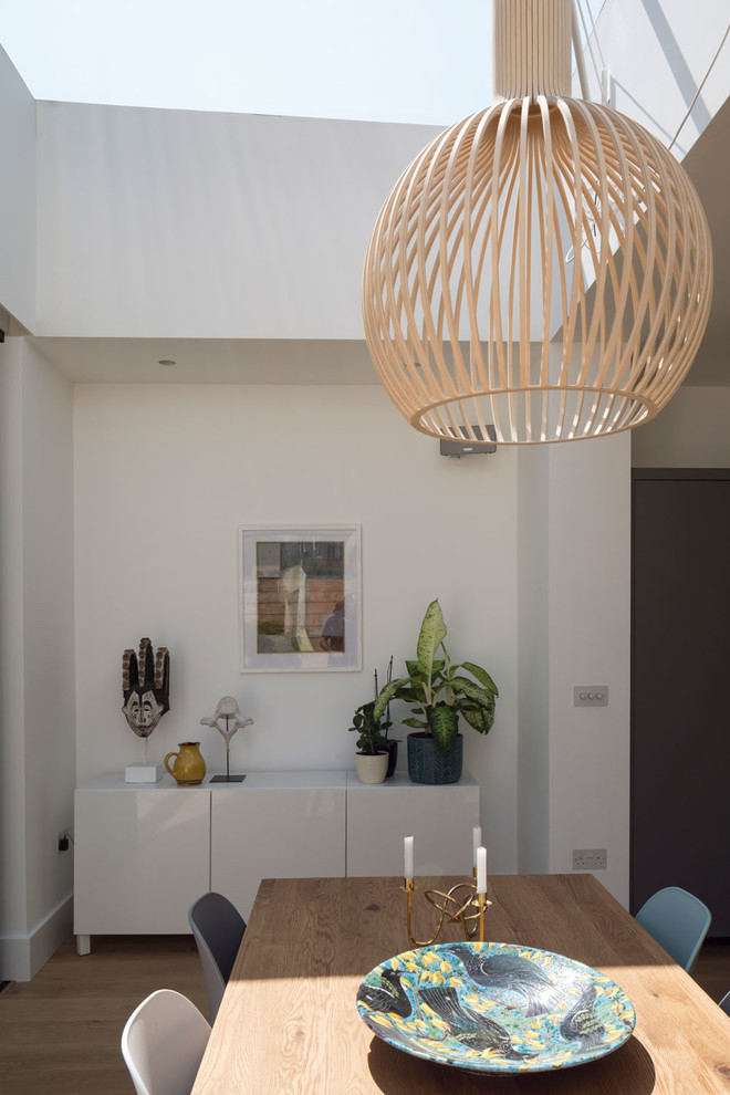 Cette image montre une grande salle à manger ouverte sur la cuisine design avec un mur blanc, parquet clair et un sol marron.