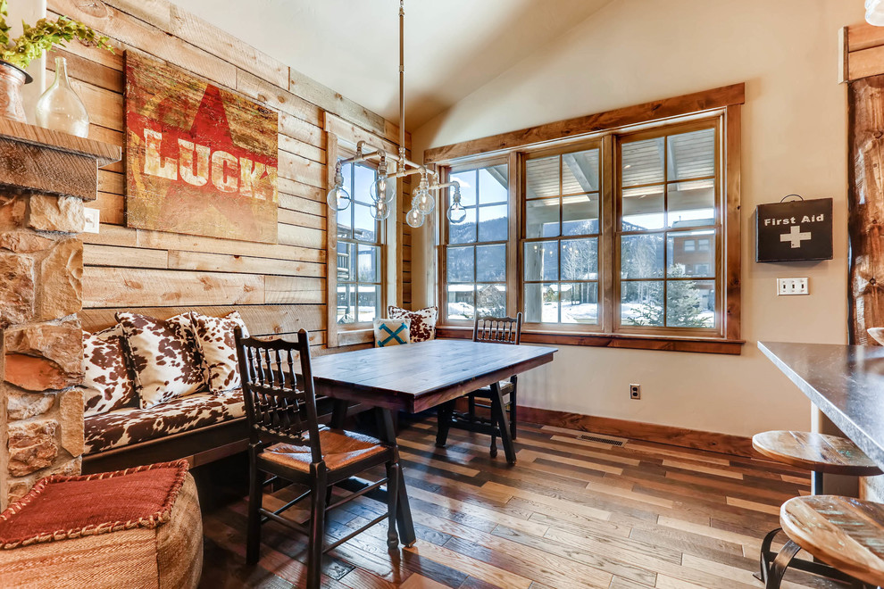 Photo of a small rustic open plan dining room in Denver with brown walls, dark hardwood flooring, a standard fireplace, a stone fireplace surround and brown floors.