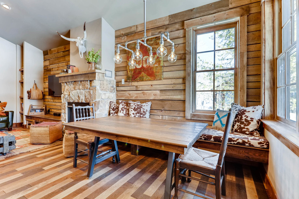 Photo of a small rustic open plan dining room in Denver with brown walls, dark hardwood flooring, a standard fireplace, a stone fireplace surround and brown floors.