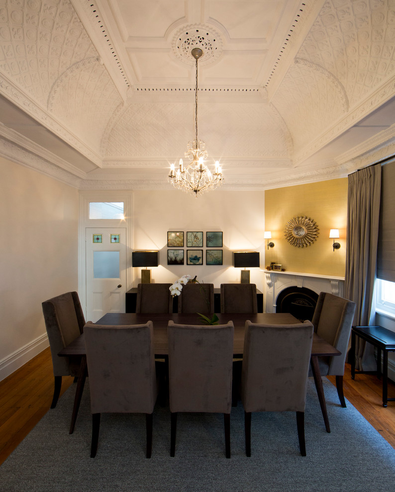 Idée de décoration pour une salle à manger ouverte sur le salon tradition de taille moyenne avec un mur jaune, un sol en bois brun, une cheminée d'angle et un manteau de cheminée en plâtre.