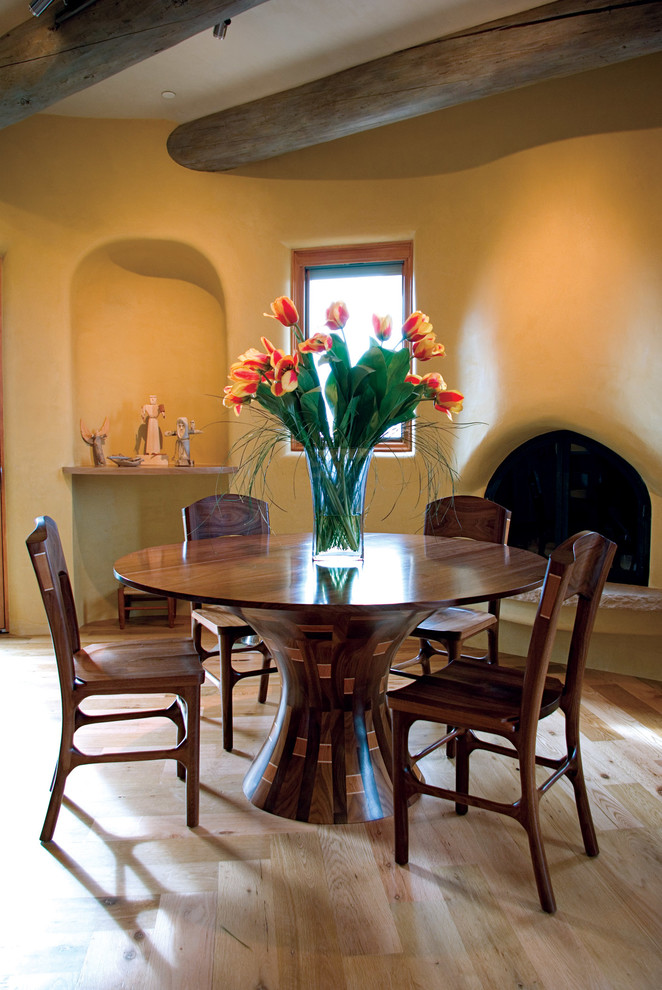 Exemple d'une salle à manger sud-ouest américain avec un mur beige, une cheminée d'angle et parquet clair.