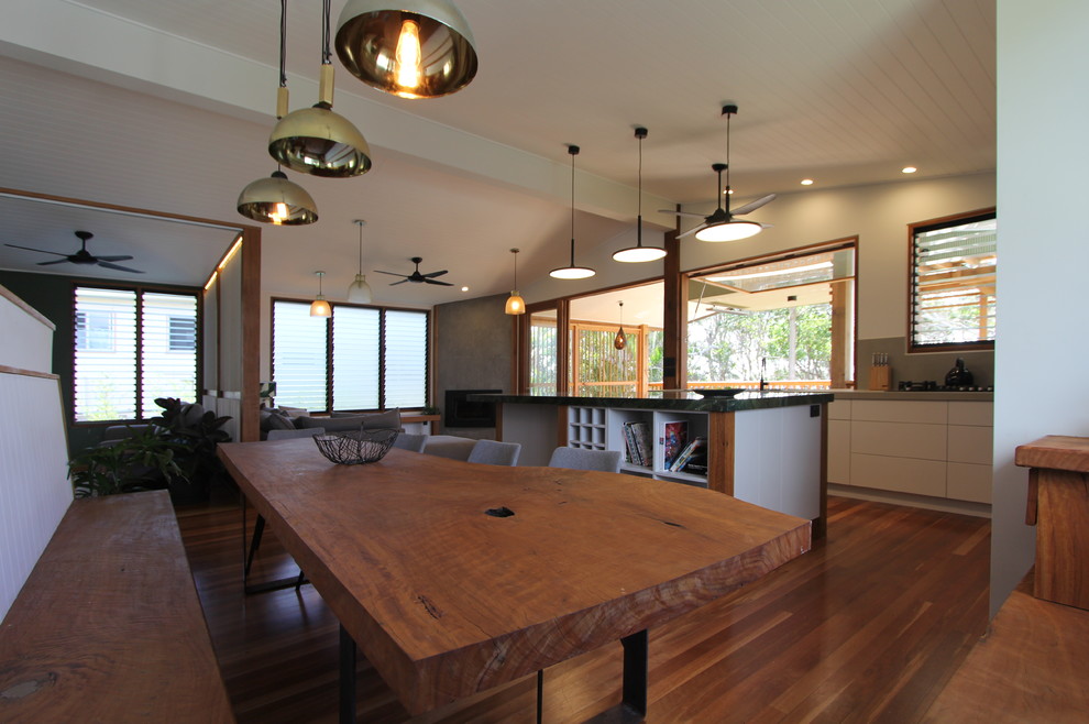 Réalisation d'une grande salle à manger ouverte sur le salon design avec un mur blanc, un sol en bois brun, une cheminée d'angle et un manteau de cheminée en plâtre.