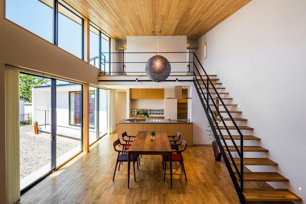 Idée de décoration pour une salle à manger ouverte sur le salon minimaliste de taille moyenne avec un mur blanc, un sol en bois brun, un sol marron et aucune cheminée.