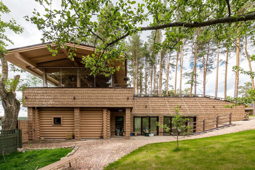 На фото: большой, коричневый частный загородный дом в стиле кантри с разными уровнями, комбинированной облицовкой и двускатной крышей с