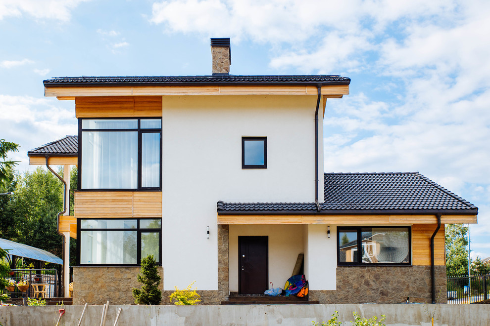 Diseño de fachada de casa blanca actual de tamaño medio de dos plantas con revestimientos combinados, tejado a dos aguas y tejado de teja de barro