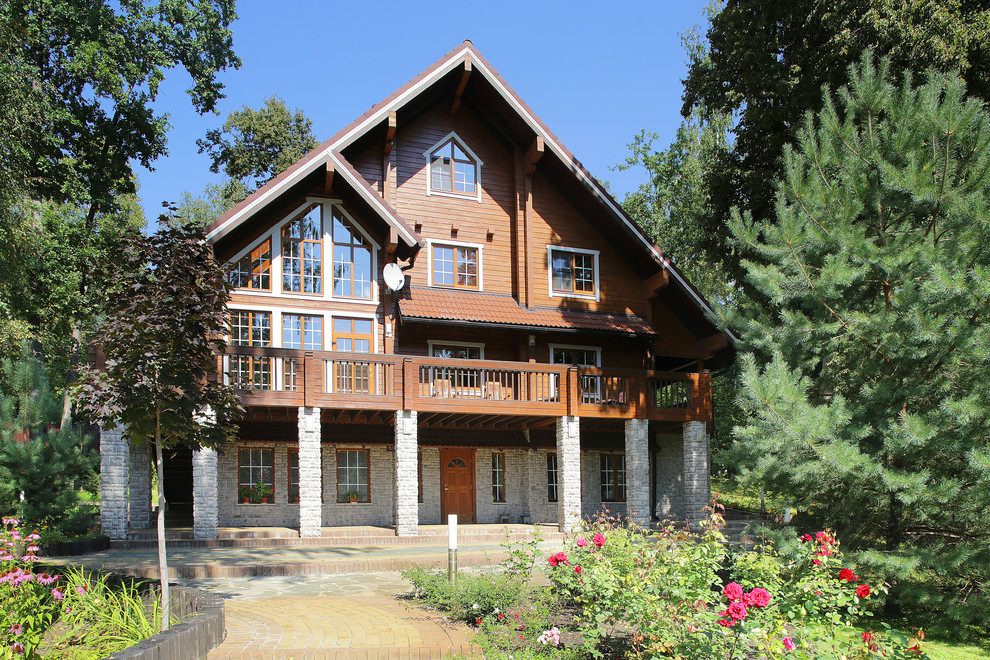 This is an example of a large and brown rustic detached house in Moscow with three floors, wood cladding, a pitched roof and a tiled roof.