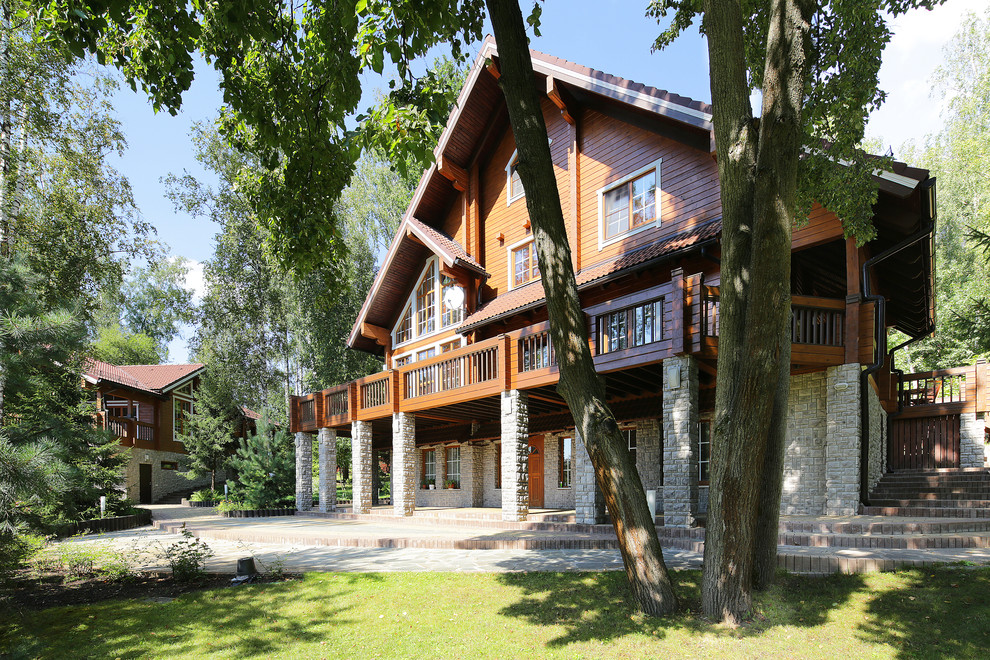 На фото: большой, трехэтажный, деревянный, коричневый частный загородный дом в стиле рустика с двускатной крышей и черепичной крышей с