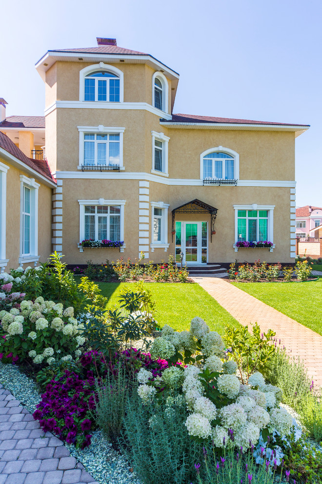 Ejemplo de fachada de casa beige mediterránea grande de tres plantas con revestimiento de estuco, tejado de metal y tejado a dos aguas