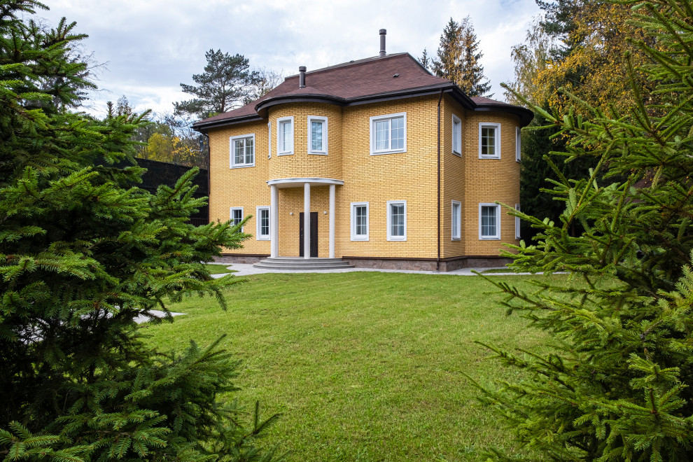 На фото: двухэтажный, кирпичный, оранжевый частный загородный дом среднего размера с коричневой крышей