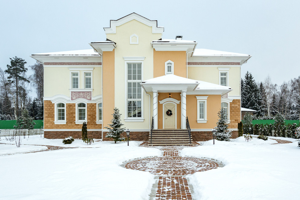 На фото: большой, двухэтажный, разноцветный частный загородный дом в классическом стиле с облицовкой из цементной штукатурки с