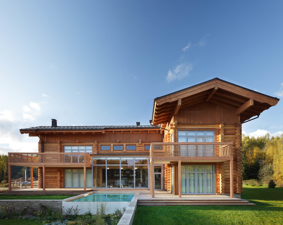 На фото: двухэтажный, деревянный дом из бревен в стиле рустика с двускатной крышей и черепичной крышей