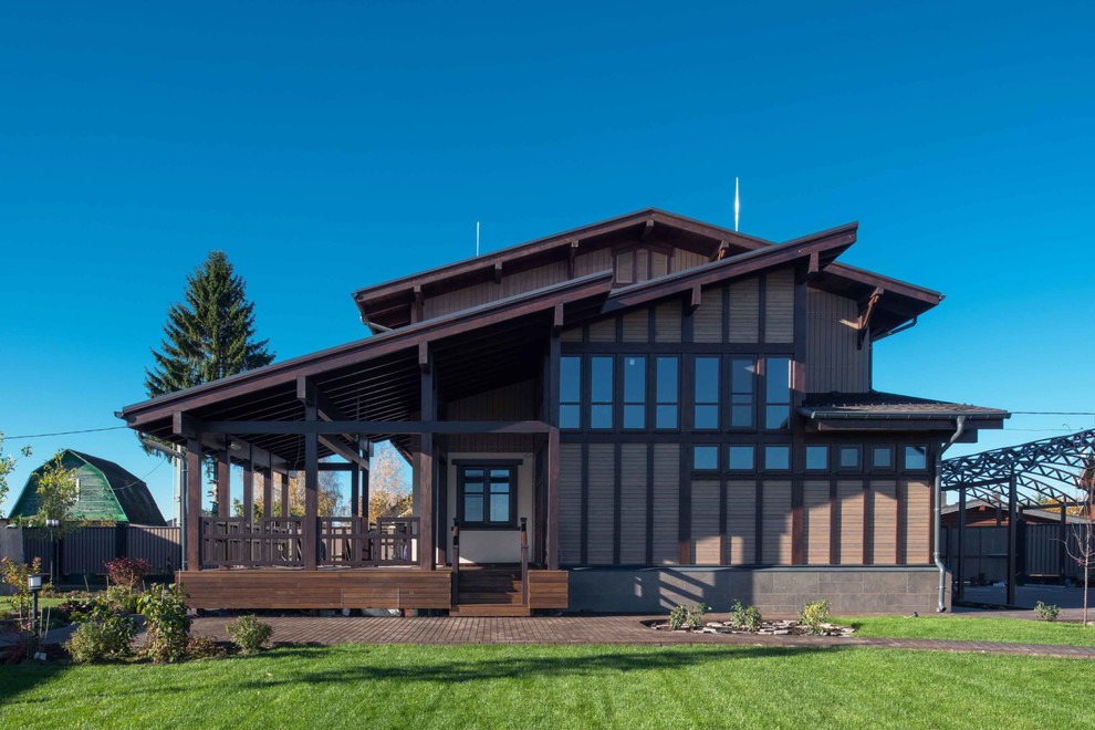 Cette photo montre une façade de maison marron chic en bois de taille moyenne et à un étage avec un toit en appentis et un toit en métal.