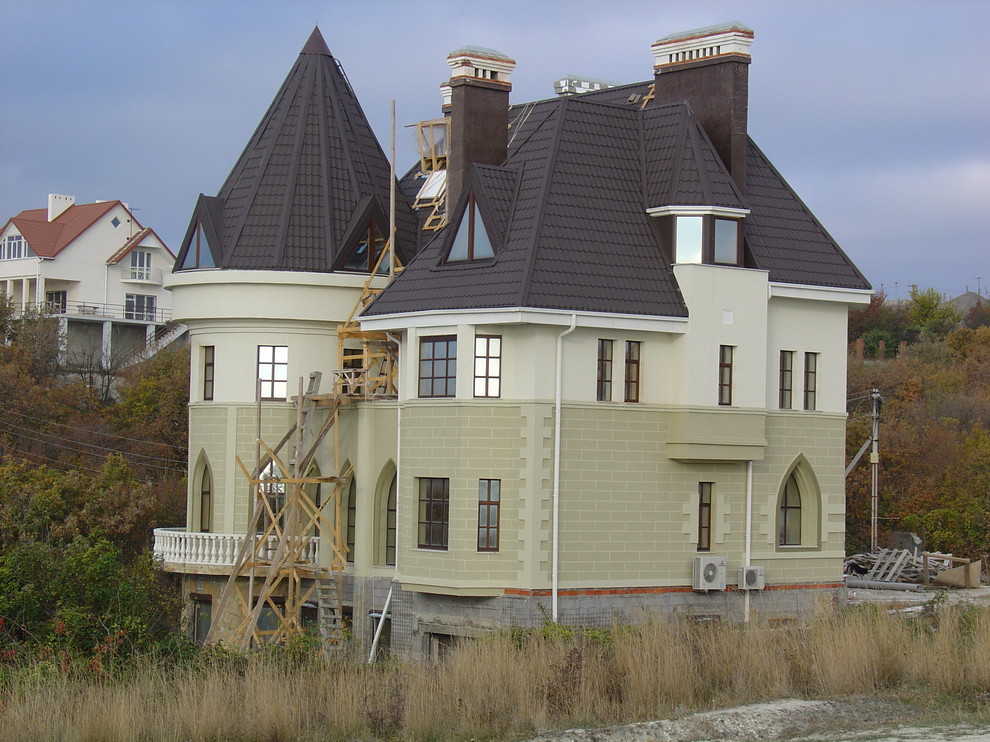 На фото: большой, трехэтажный, бежевый частный загородный дом в стиле рустика с облицовкой из камня, вальмовой крышей и черепичной крышей с