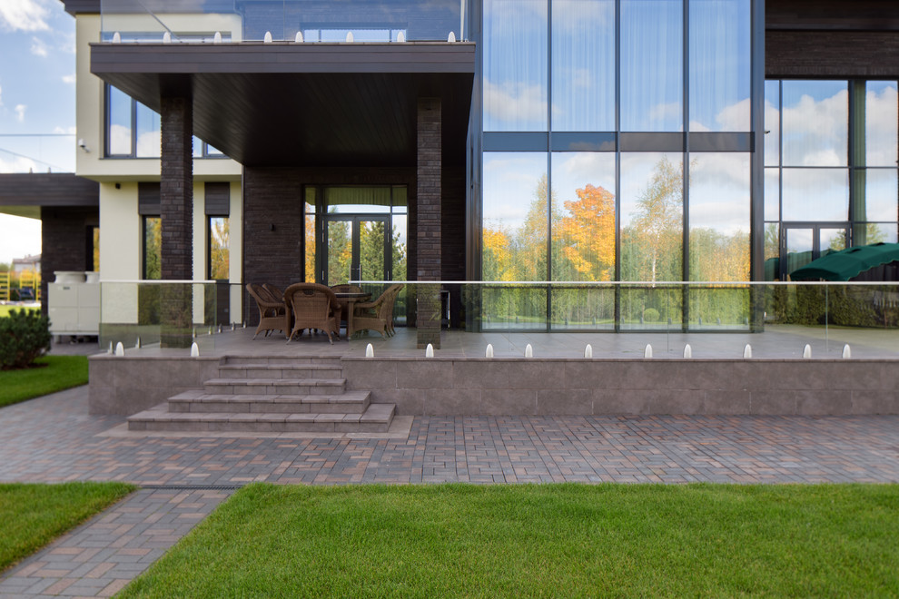 Idéer för en stor modern veranda på baksidan av huset, med utekök, naturstensplattor, takförlängning och räcke i glas