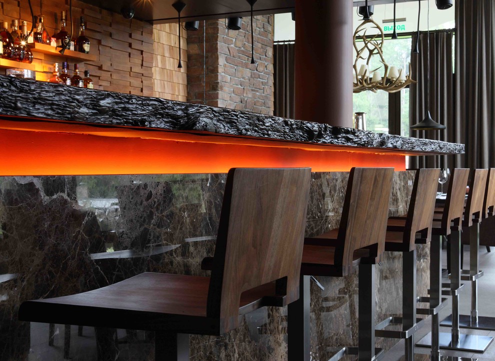 На фото: угловой домашний бар среднего размера в современном стиле с барной стойкой, деревянной столешницей, полом из сланца, серым полом и коричневой столешницей с