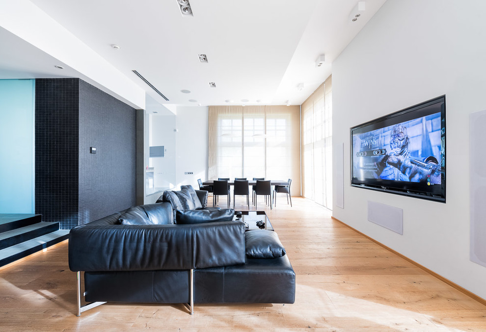 Стильный дизайн: большой открытый домашний кинотеатр в современном стиле с белыми стенами, деревянным полом и телевизором на стене - последний тренд
