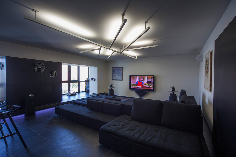 Réalisation d'une grande salle de cinéma design ouverte avec un mur blanc, un sol en ardoise, un téléviseur fixé au mur et un sol noir.