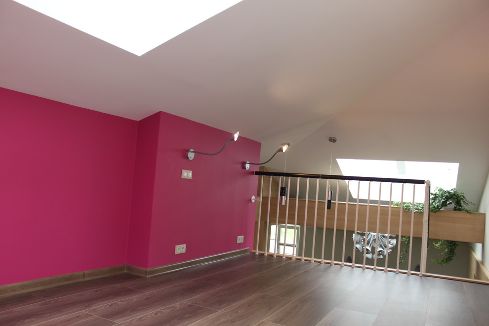 Immagine di un piccolo home theatre minimal aperto con pareti rosa, pavimento in laminato, TV a parete e pavimento marrone