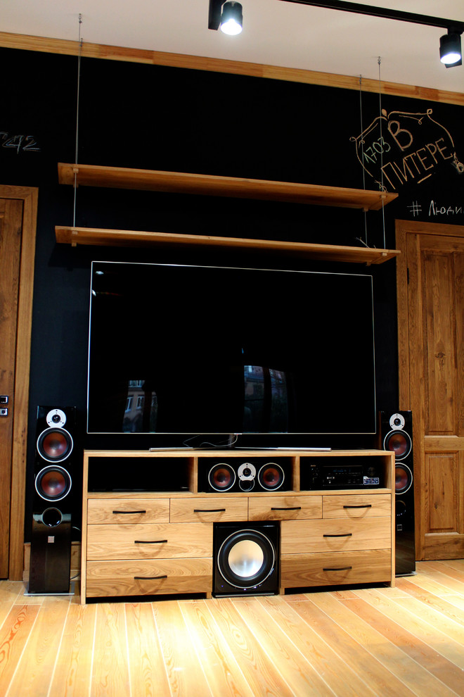 Modelo de cine en casa nórdico de tamaño medio con paredes negras, suelo de madera clara y pared multimedia