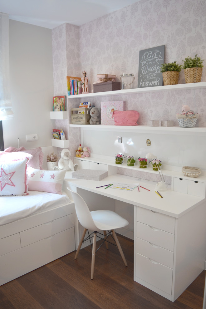 Modelo de habitación de niña de 4 a 10 años tradicional renovada de tamaño medio con escritorio, paredes rosas, suelo de madera en tonos medios y suelo beige