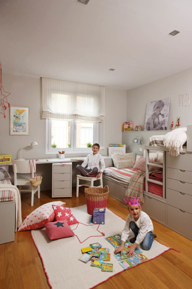 Medium sized traditional gender neutral children’s room in Madrid with beige walls and medium hardwood flooring.