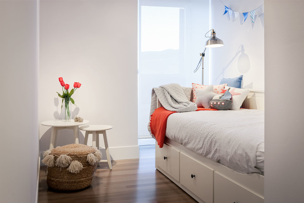 Idéer för mellanstora funkis könsneutrala barnrum kombinerat med sovrum och för 4-10-åringar, med vita väggar och mellanmörkt trägolv