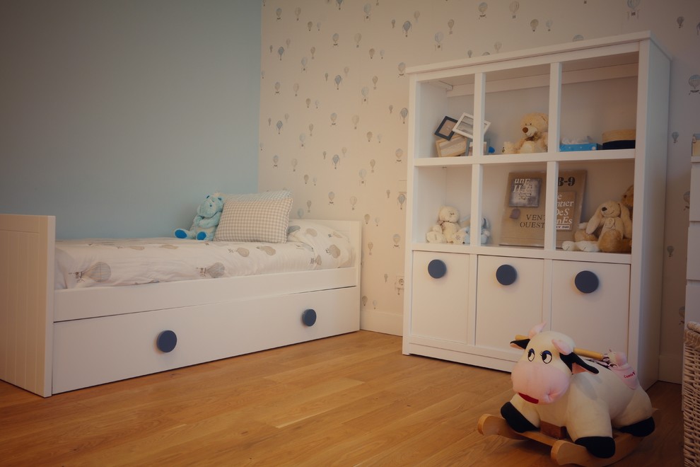 Medium sized traditional gender neutral toddler’s room in Madrid with multi-coloured walls and medium hardwood flooring.