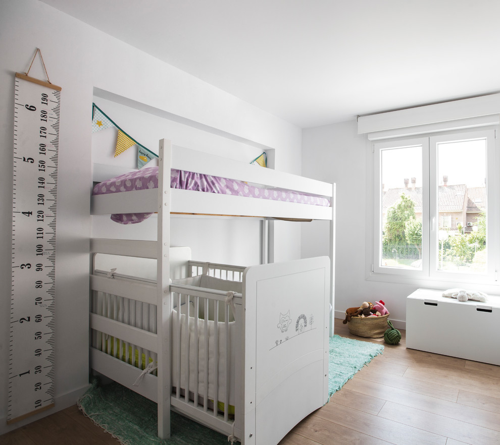 Immagine di una cameretta per bambini da 1 a 3 anni minimal con pareti bianche, pavimento in legno massello medio e pavimento marrone