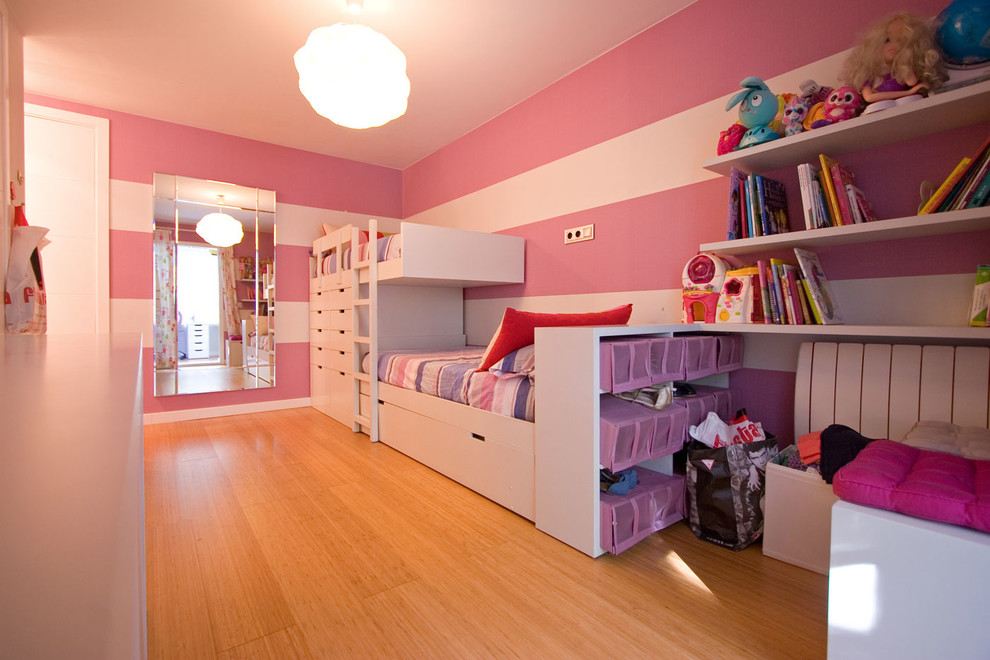 This is an example of a large contemporary children’s room for girls in Seville with pink walls and medium hardwood flooring.