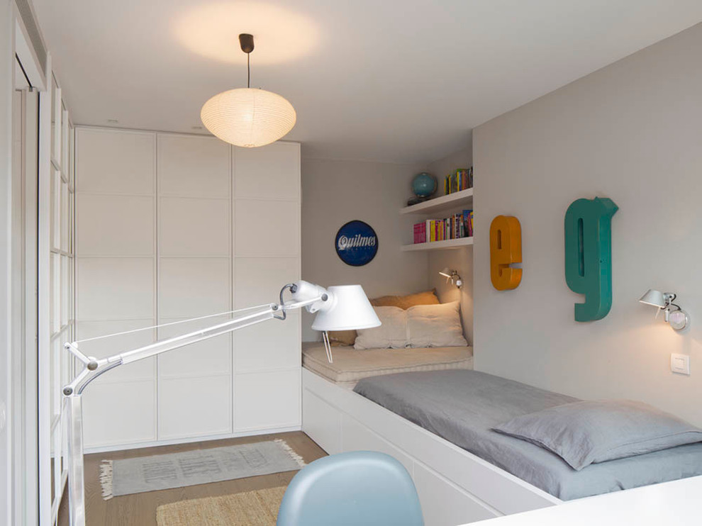 This is an example of a medium sized scandi gender neutral children’s room in Barcelona with white walls and medium hardwood flooring.