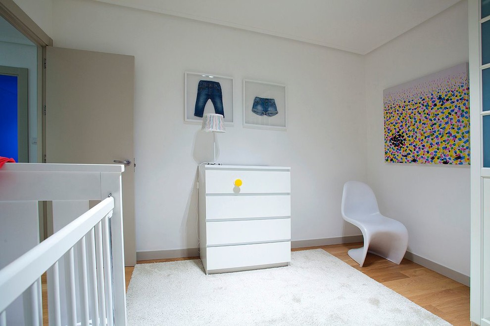 Immagine di una cameretta per bambini da 1 a 3 anni design di medie dimensioni con pareti bianche e pavimento in legno massello medio