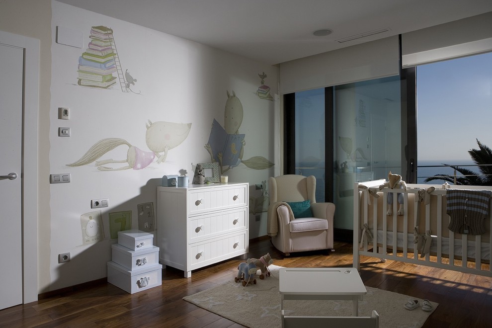 Immagine di una cameretta per bambini da 1 a 3 anni tradizionale di medie dimensioni con pareti bianche e pavimento in legno massello medio