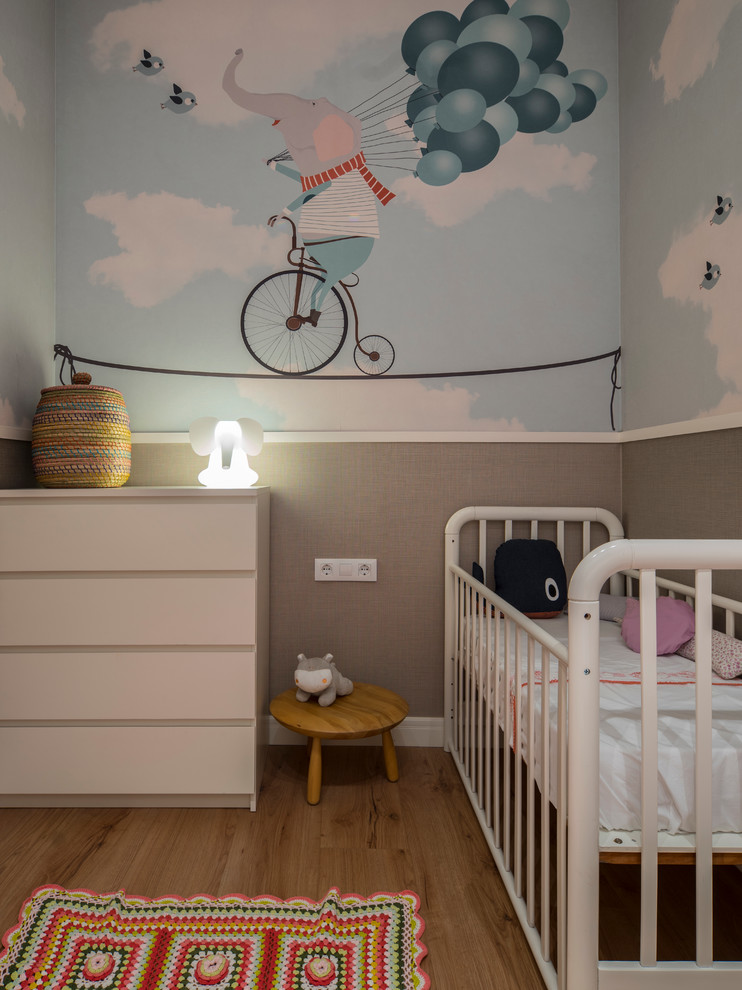 Imagen de habitación de bebé niña de tamaño medio con paredes multicolor y suelo de madera en tonos medios