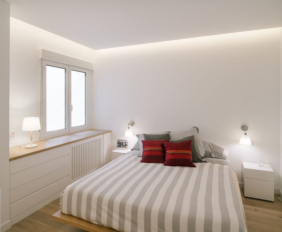 Mittelgroßes Skandinavisches Hauptschlafzimmer ohne Kamin mit weißer Wandfarbe und braunem Holzboden in Madrid