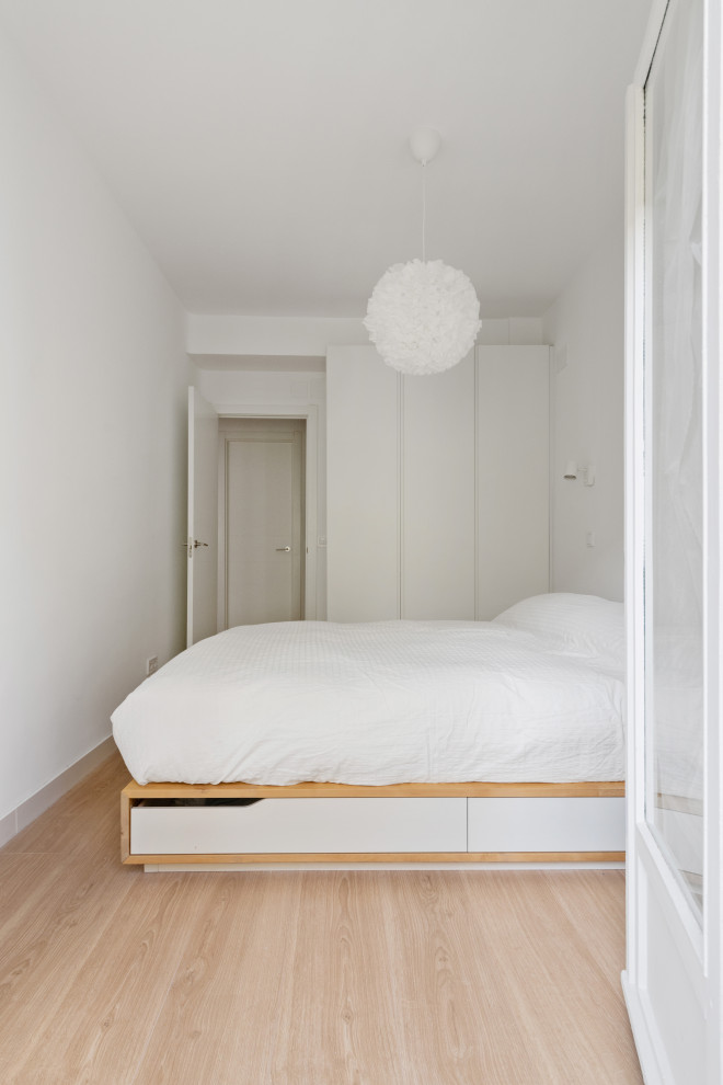 This is an example of a small modern master bedroom in Madrid with white walls, light hardwood flooring and beige floors.