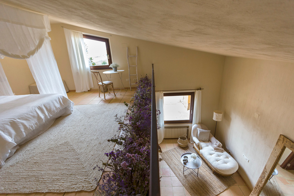 Ejemplo de dormitorio tipo loft campestre grande sin chimenea con paredes beige y suelo de baldosas de terracota