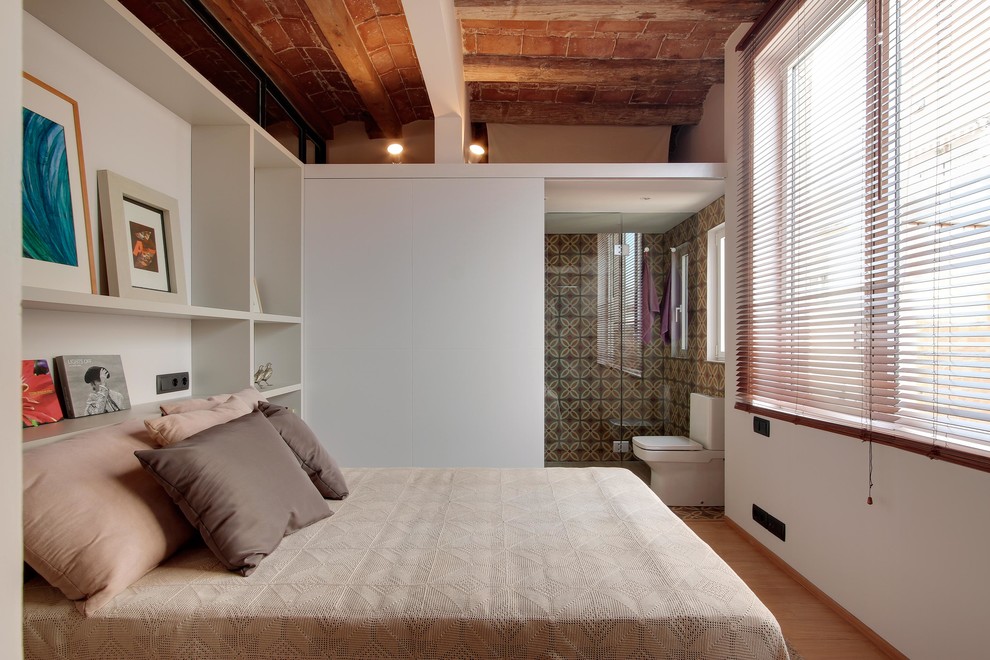 Modelo de dormitorio principal urbano de tamaño medio sin chimenea con paredes blancas y suelo de madera clara