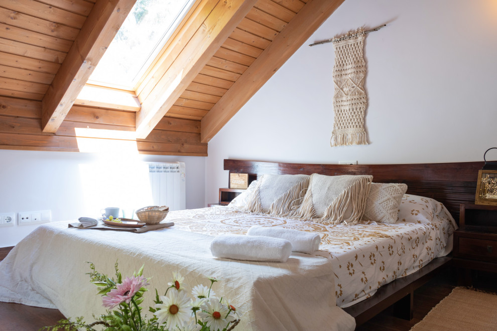 Modelo de dormitorio principal rústico de tamaño medio con paredes blancas, suelo de madera oscura y suelo marrón