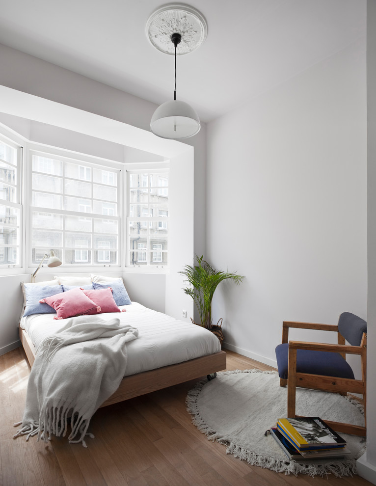 Modelo de dormitorio contemporáneo sin chimenea con suelo de madera en tonos medios y paredes blancas