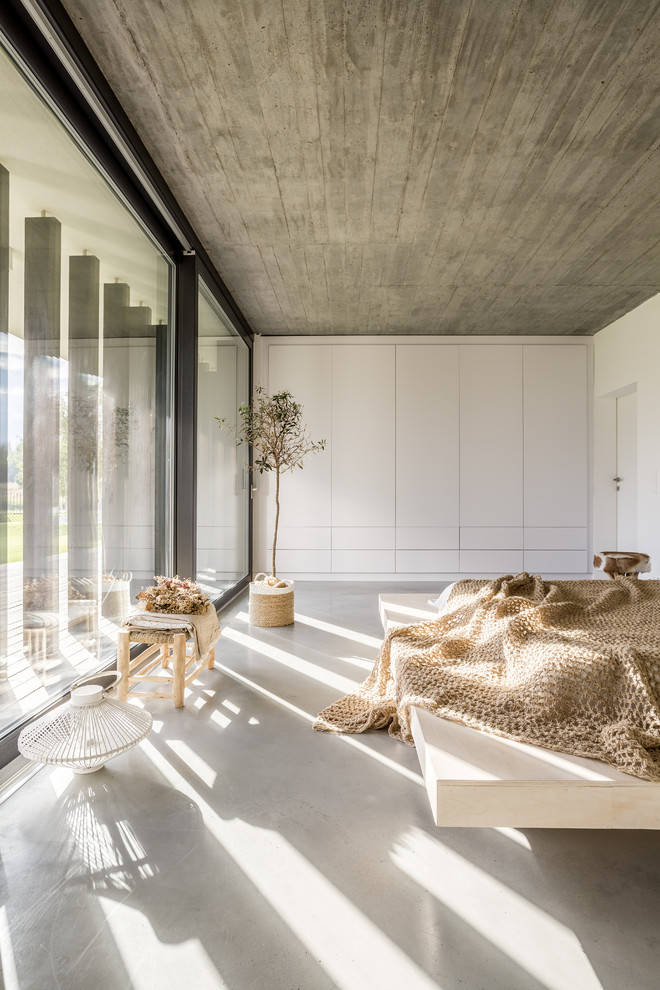 Modern bedroom in Other with white walls, concrete flooring and grey floors.