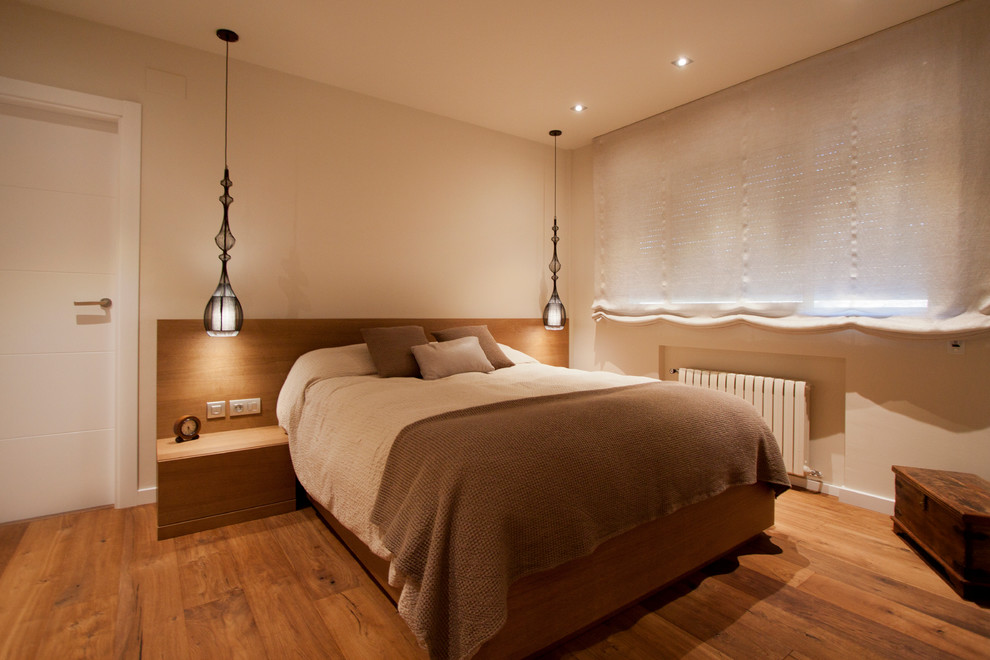 Cette image montre une chambre parentale design de taille moyenne avec un mur beige, un sol en bois brun et aucune cheminée.
